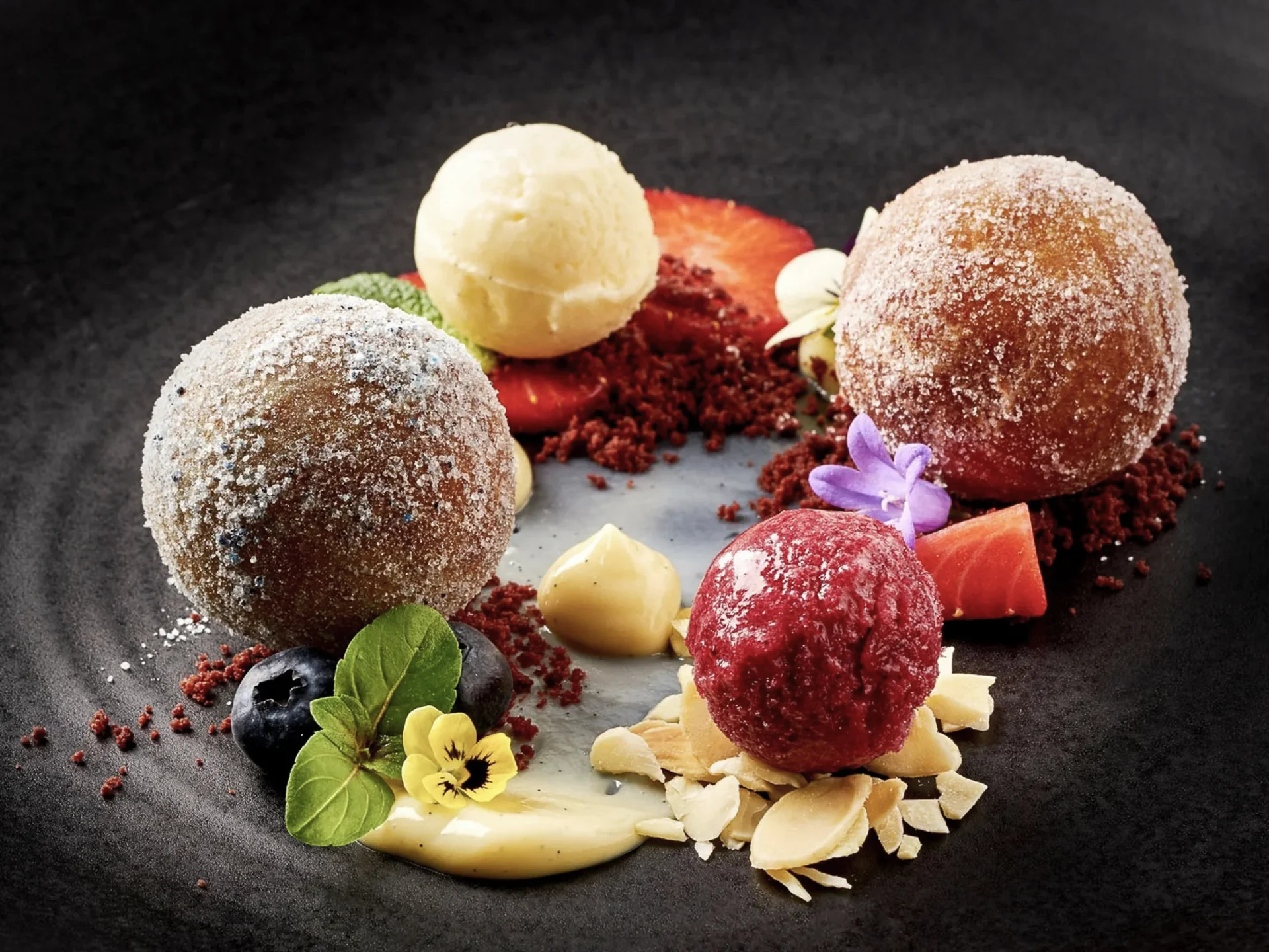 Die Bilder aus dem Hotel Salnerhof Kunstvoll angerichtetes Dessert mit Kugeln, Beeren, Blüten und Creme auf schwarzem Teller