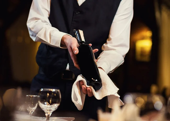Der Salnerhof – das Hotel in Ischgl Kellner hält eine Weinflasche und wischt sie mit einem weißen Tuch ab