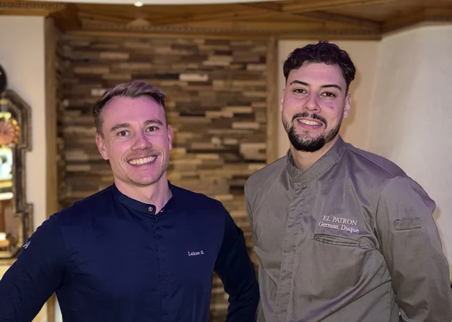 Dein Job im Salnerhof Zwei lächelnde Männer in Kochjacken vor einem rustikalen Hintergrund im Restaurant