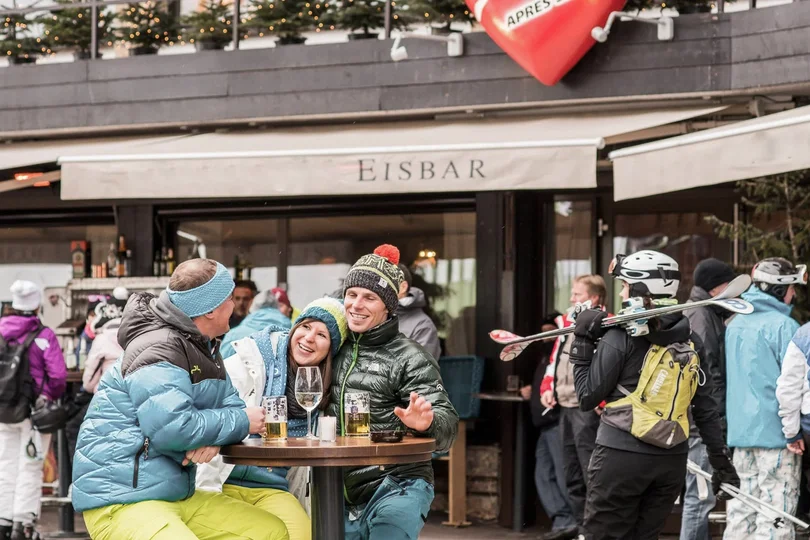 Silvretta Skigebiet Menschen in Winterkleidung sitzen und stehen vor einer Eisbar mit Getränken