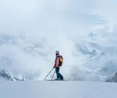 Silvretta Skigebiet Skifahrer mit Helm und Rucksack auf verschneitem Berg vor nebligen Bergen