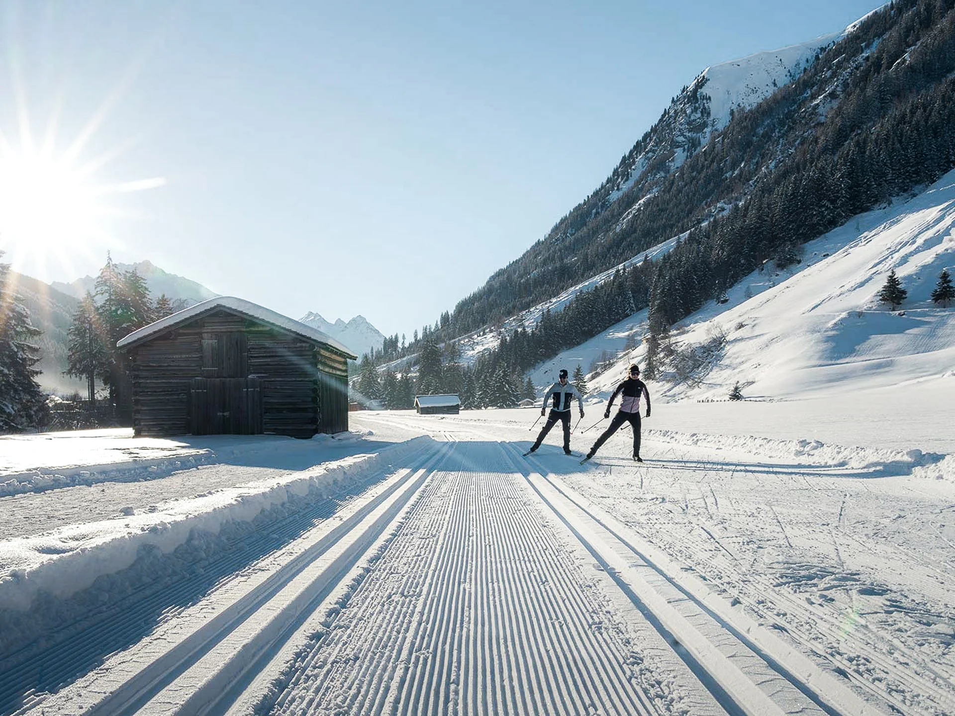 Die Bilder aus dem Hotel Salnerhof Zwei Langläufer auf präparierter Spur in verschneitem Tal mit Holzhütte und Bergen