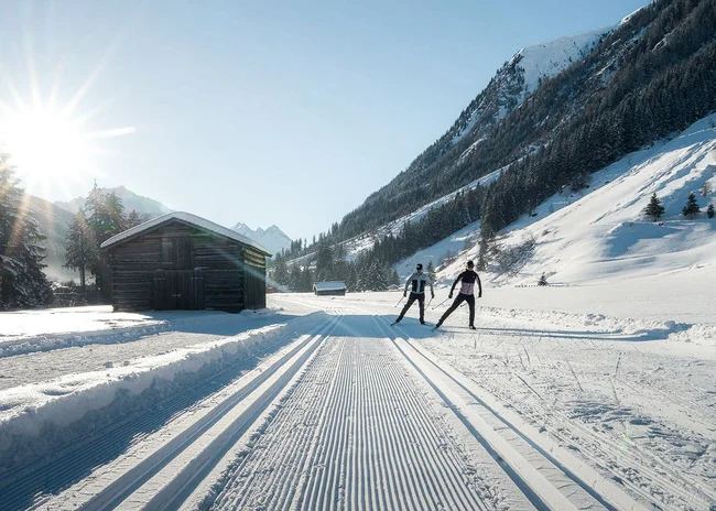 Der Salnerhof – das Hotel in Ischgl Zwei Langläufer auf präparierter Spur in verschneitem Tal mit Holzhütte und Bergen