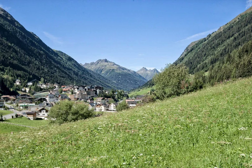 Ihre Anreise zum Salnerhof in Ischgl Bergdorf in einem grünen Tal mit Wiesen und bewaldeten Bergen bei klarem Himmel