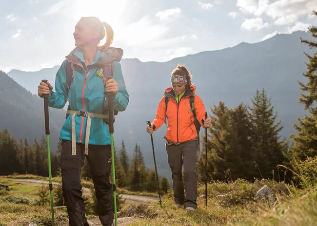 Ihr Sommer im Paznaun im Wander- und Bike-Hotel in Ischgl Zwei Frauen wandern mit Trekkingstöcken in den Bergen bei Sonnenschein