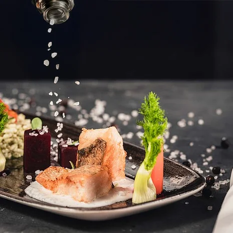 Geschmack Gourmetgericht mit Fisch, Gemüse und grobem Salz auf schwarzem Teller