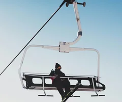 Silvretta Skigebiet Person sitzt auf einem Skilift mit Skiern vor klarem blauem Himmel und Bergkulisse