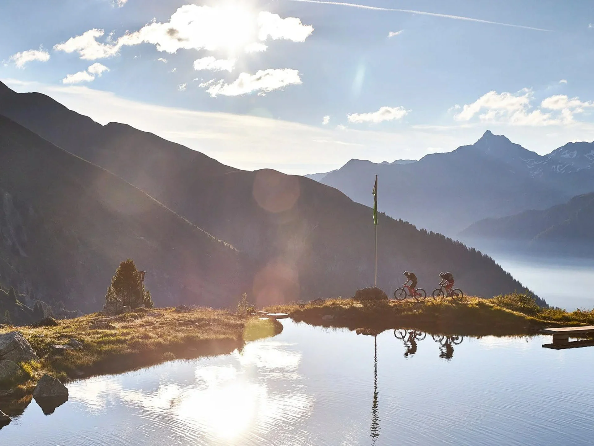 Die Bilder aus dem Hotel Salnerhof Zwei Radfahrer fahren entlang eines Bergsees bei Sonnenuntergang mit Bergen im Hintergrund