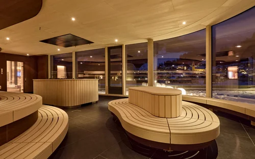 Moderner Ruheraum mit geschwungenen Holzsitzen und Panoramafenstern bei Nacht
