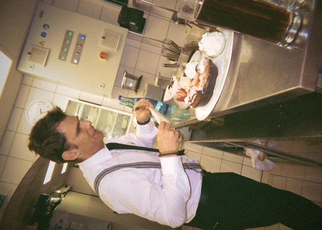 Dein Job im Salnerhof Mann in weißem Hemd bereitet Dessert mit Sahne in professioneller Küche zu