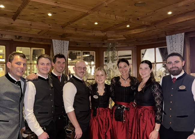 Dein Job im Salnerhof Gruppenfoto von Hotelmitarbeitern in traditioneller Tracht in einem Holzinterieur