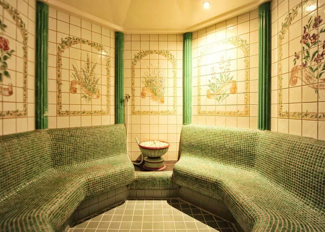 Der Salnerhof – das Hotel in Ischgl Saunaraum mit grünen Mosaikbänken und dekorativen Wandfliesen mit Blumenmotiven