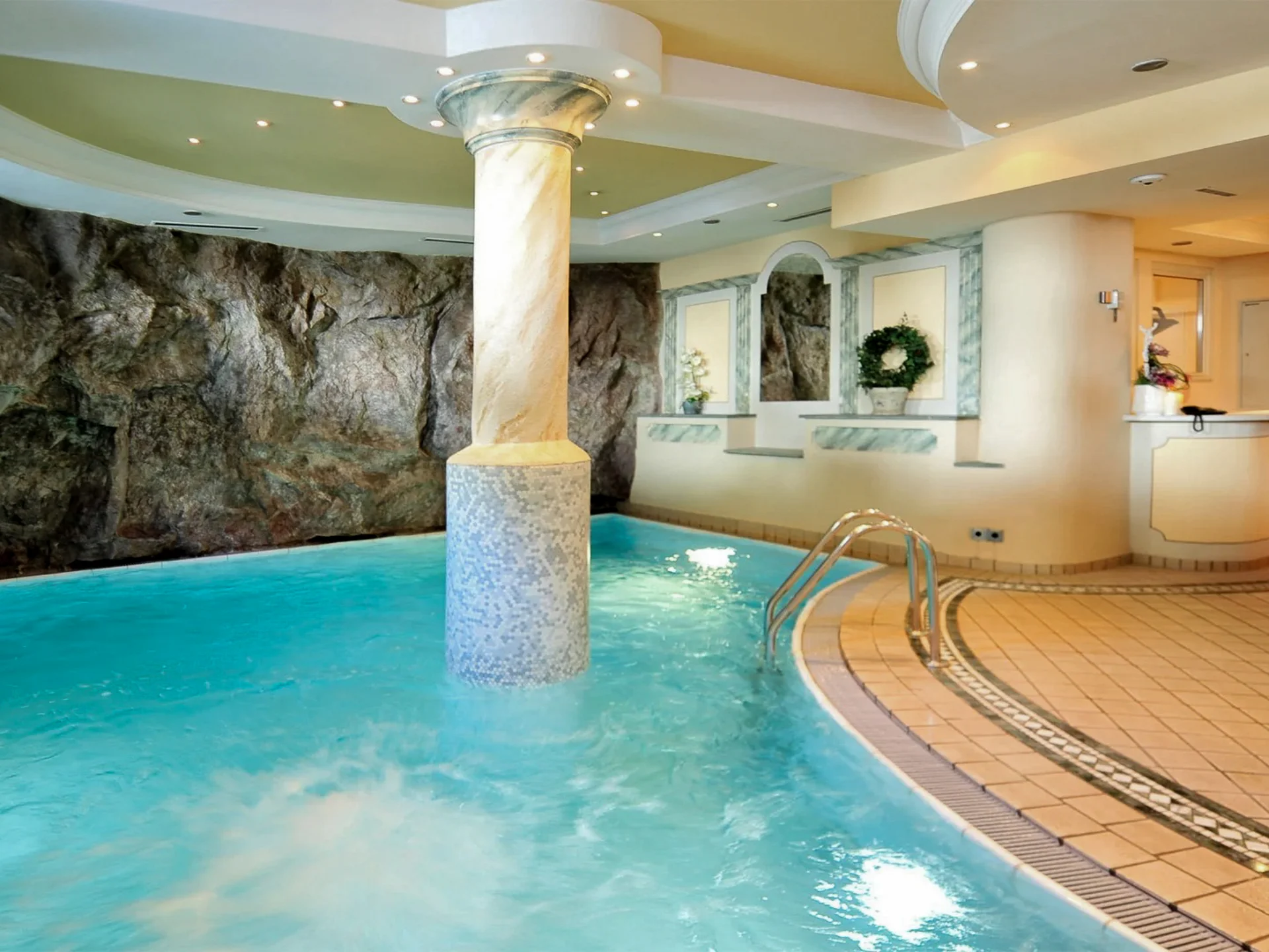 Die Bilder aus dem Hotel Salnerhof Innenpool mit Säule, Felswand und Empfangstresen in einem Wellnessbereich