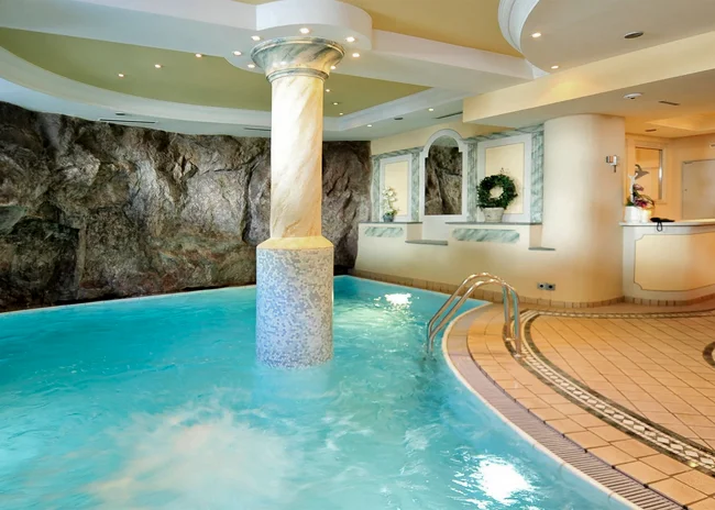 Der Salnerhof – das Hotel in Ischgl Innenpool mit Säule, Felswand und Empfangstresen in einem Wellnessbereich