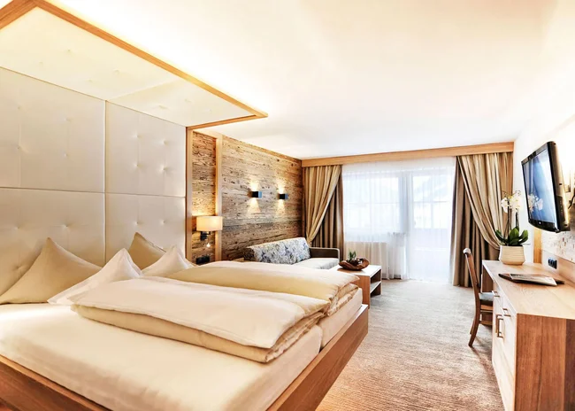 Der Salnerhof – das Hotel in Ischgl Modernes Hotelzimmer mit Doppelbett, Sofa und großem Fenster mit Vorhängen