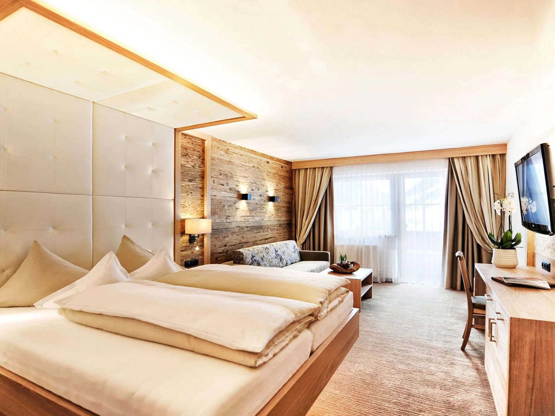Die Bilder aus dem Hotel Salnerhof Modernes Hotelzimmer mit Doppelbett, Sofa und großem Fenster mit Vorhängen