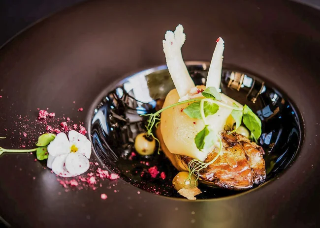 Ihr liebstes Restaurant in Ischgl Kunstvoll angerichtetes Gourmetgericht mit essbaren Blüten und Kräutern auf schwarzem Teller