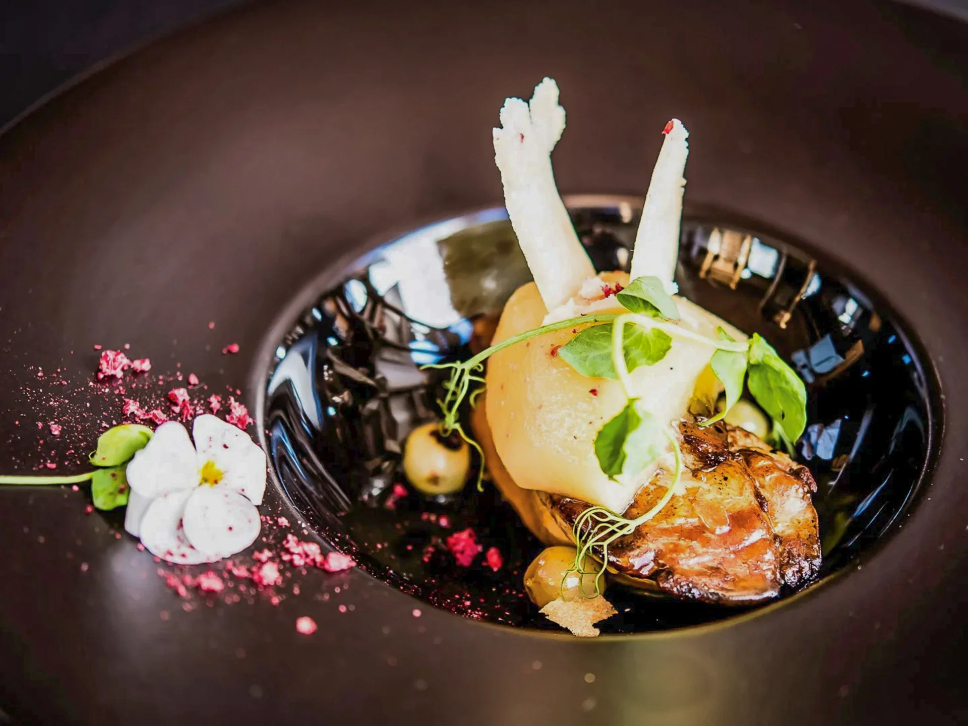 Die Bilder aus dem Hotel Salnerhof Kunstvoll angerichtetes Gourmetgericht mit essbaren Blüten und Kräutern auf schwarzem Teller