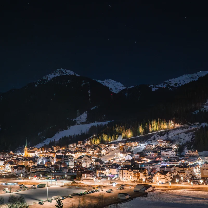 Ischgl Beleuchtetes Bergdorf bei Nacht mit schneebedeckten Gipfeln im Hintergrund