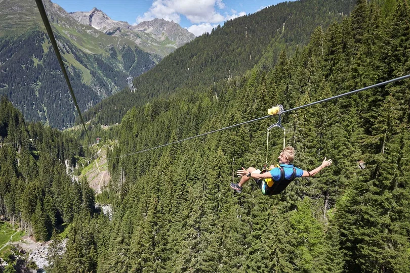 Ihr Sommer im Paznaun im Wander- und Bike-Hotel in Ischgl Person fährt auf einer Seilrutsche über einen bewaldeten Bergtalhang