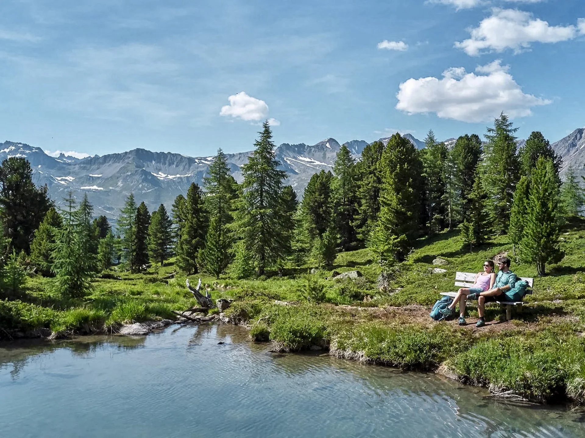 Die Bilder aus dem Hotel Salnerhof Zwei Wanderer sitzen auf einer Bank am See mit Bergpanorama und Tannen