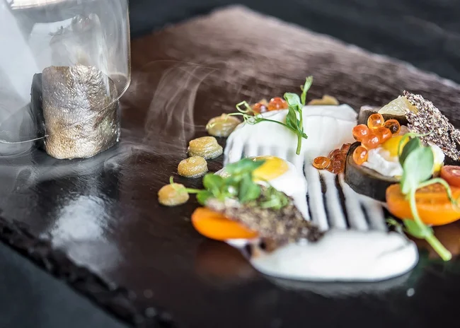 Ihr liebstes Restaurant in Ischgl Kreativ angerichtetes Gourmetgericht mit Ei, Tomaten und Saucen auf schwarzem Stein