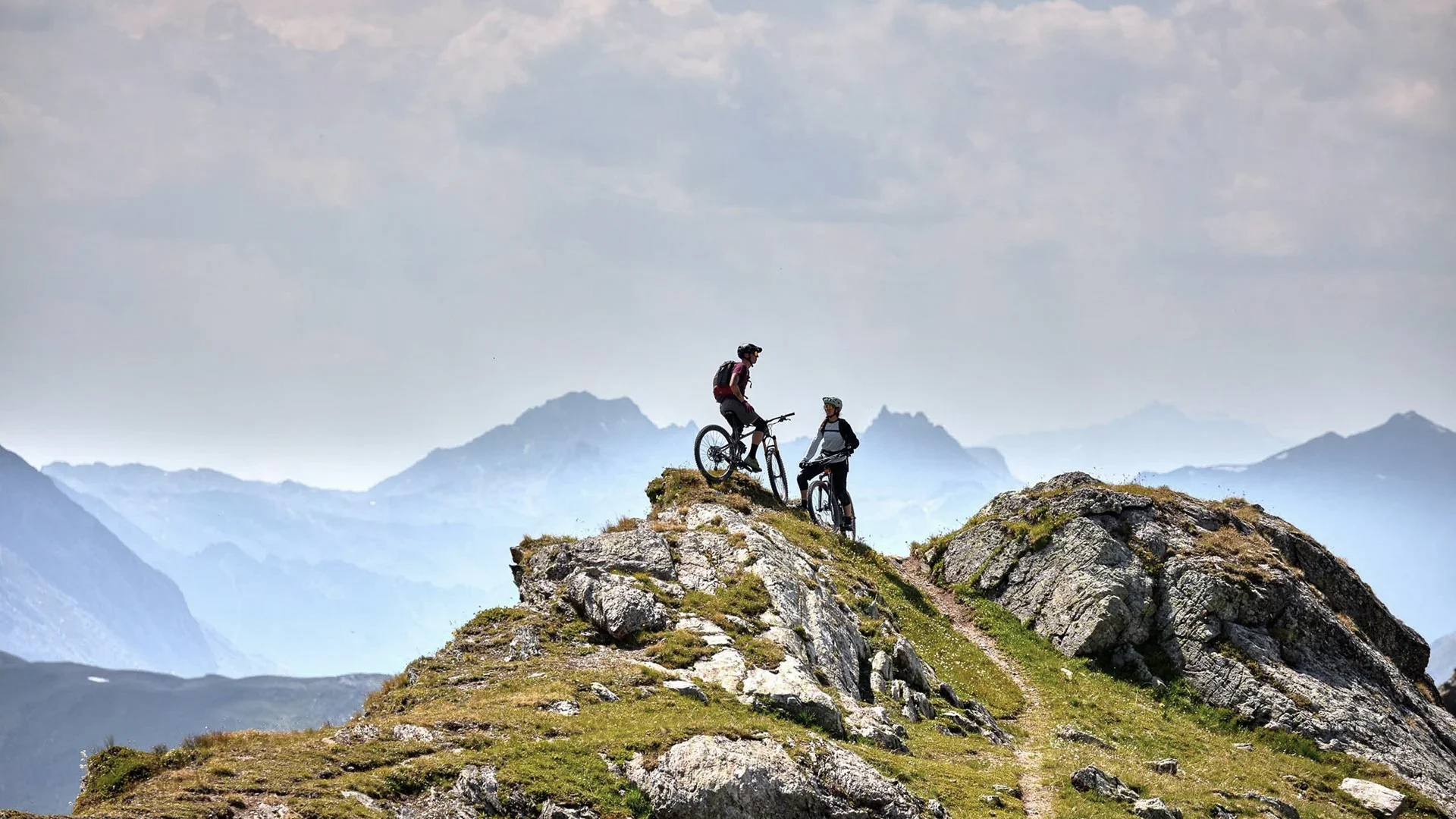 Ihr Sommer im Paznaun im Wander- und Bike-Hotel in Ischgl Zwei Mountainbiker stehen mit ihren Fahrrädern auf einem felsigen Berggipfel
