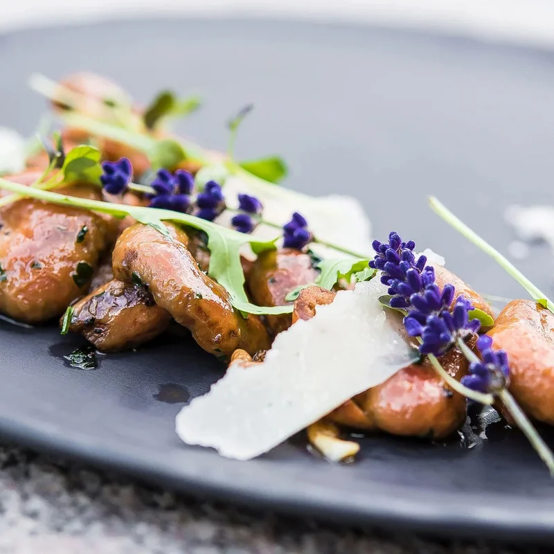Gourmetgericht mit Pilzen, Parmesan, Rucola und Lavendel auf schwarzem Teller