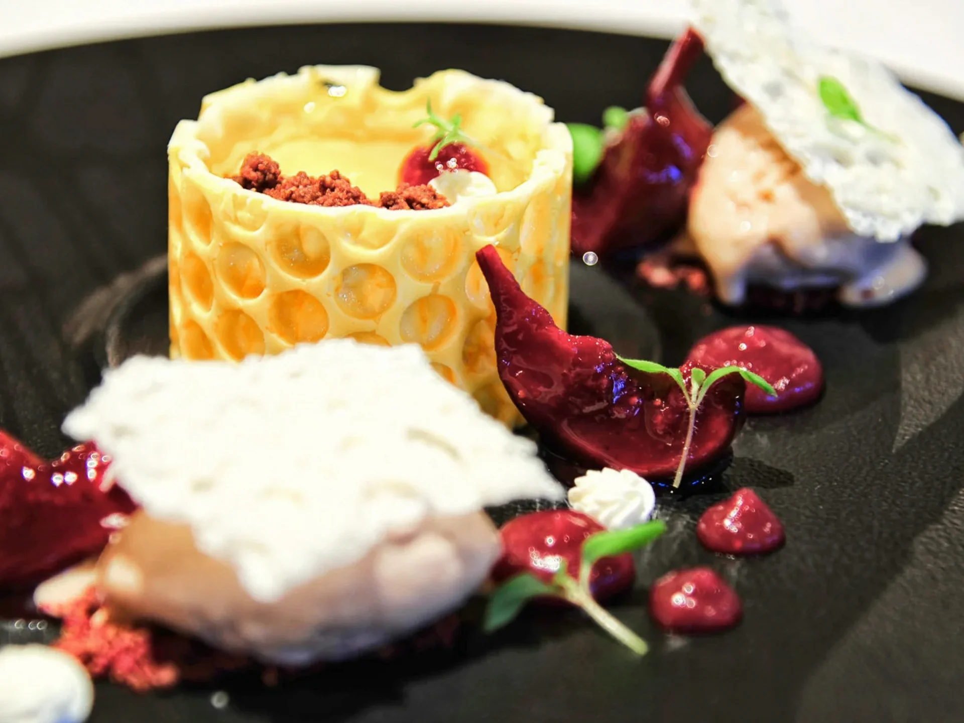 Die Bilder aus dem Hotel Salnerhof Kunstvoll angerichtetes Dessert mit Creme, roten Soßen und essbaren Dekorationen auf schwarzem Teller