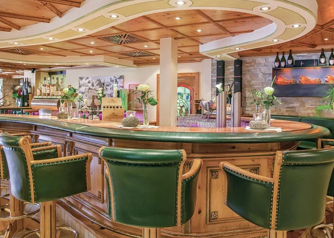 Der Salnerhof – das Hotel in Ischgl Gemütliche Bar mit grünen Ledersesseln und Holzdecke in warmem Ambiente