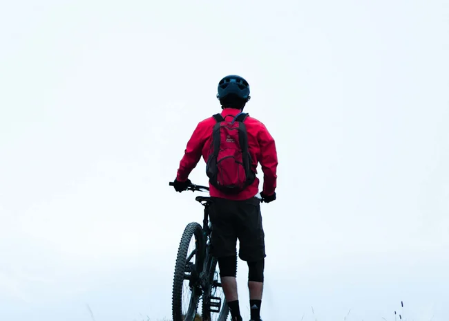 Ihr Sommer im Paznaun im Wander- und Bike-Hotel in Ischgl Mountainbiker mit rotem Rucksack steht auf Hügel mit Fahrrad