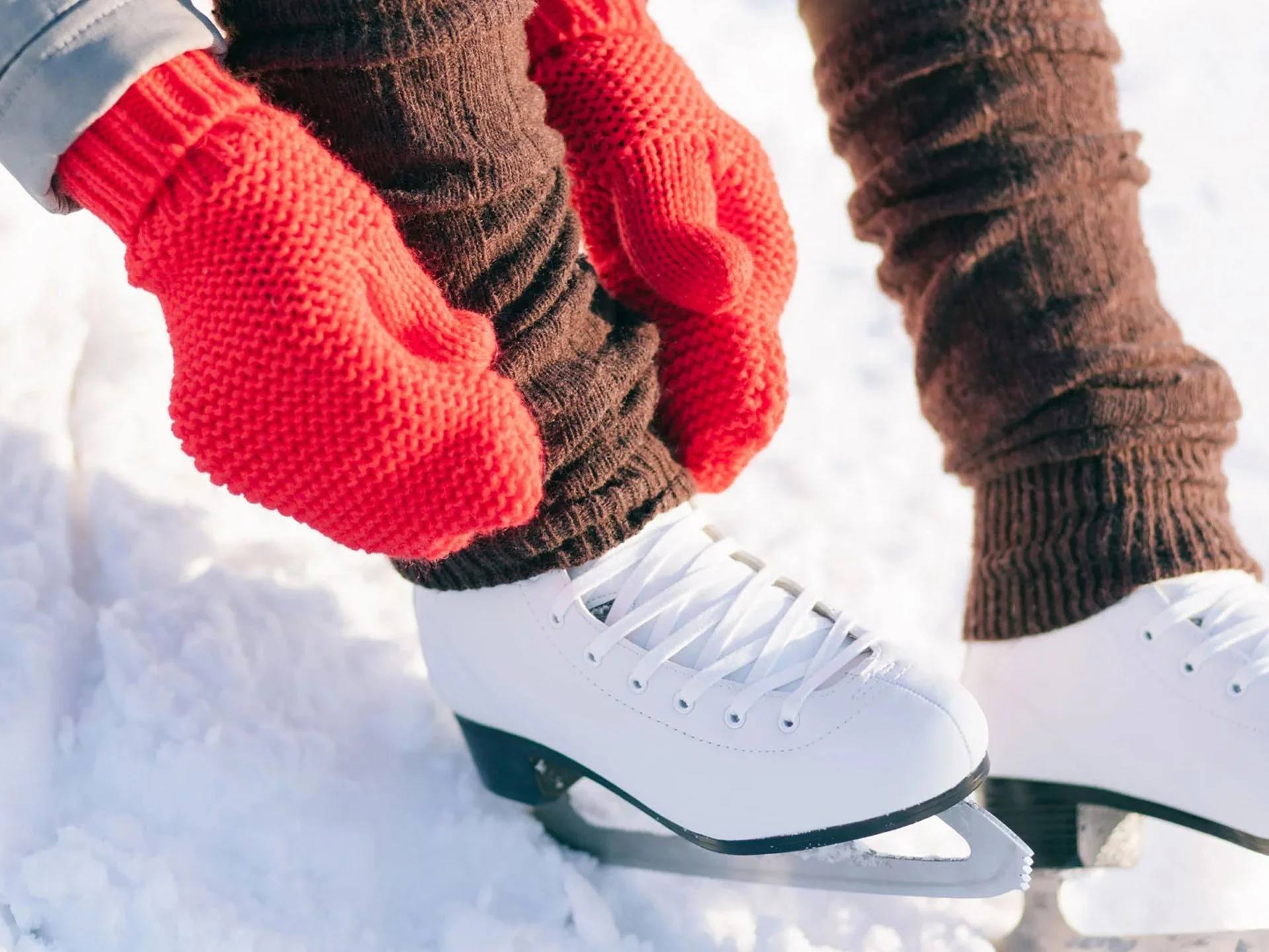 Die Bilder aus dem Hotel Salnerhof Person zieht braune Strümpfe mit roten Handschuhen über weiße Schlittschuhe im Schnee an
