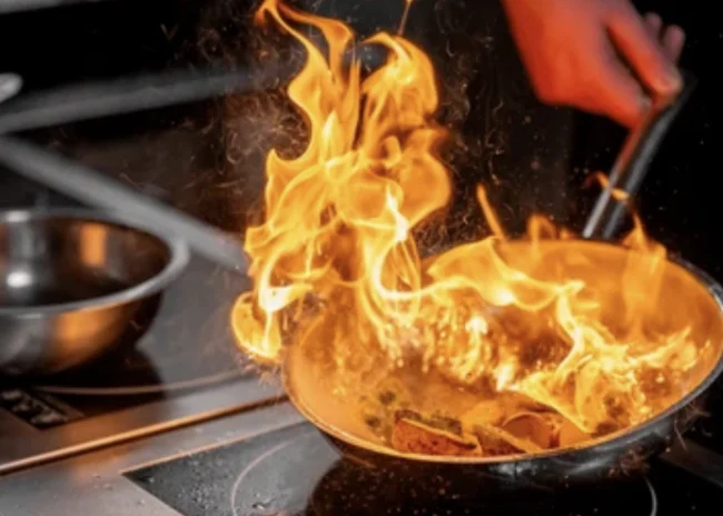 Kellner mit Inkasso Flammen schlagen aus einer Pfanne beim Kochen auf einem Herd