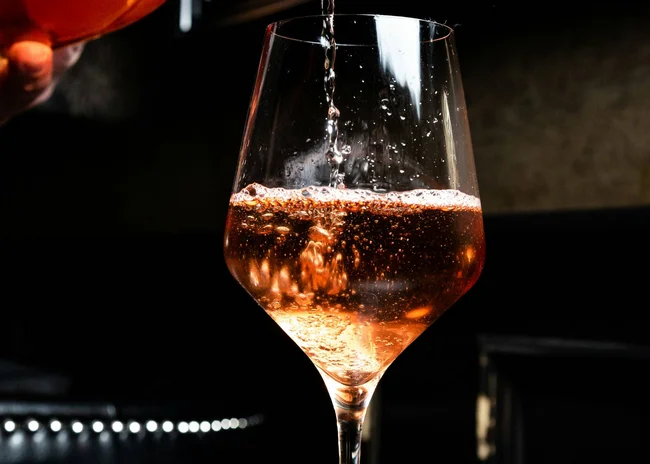 Kellner mit Inkasso Roséwein wird aus einer Flasche in ein Weinglas eingeschenkt