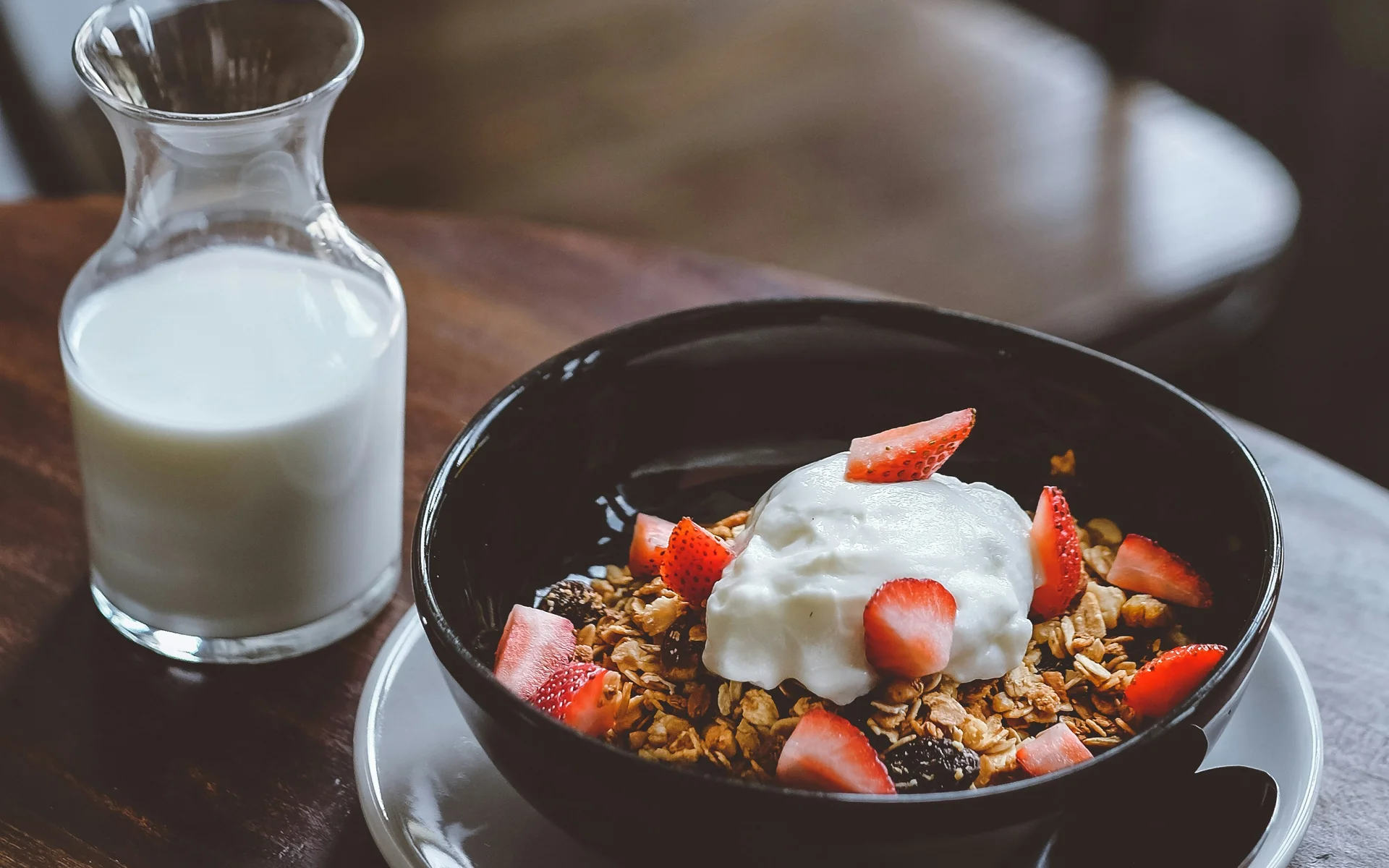 Zimmer Schüssel mit Müsli, Joghurt und Erdbeerstücken auf einem Tisch mit Milchkaraffe