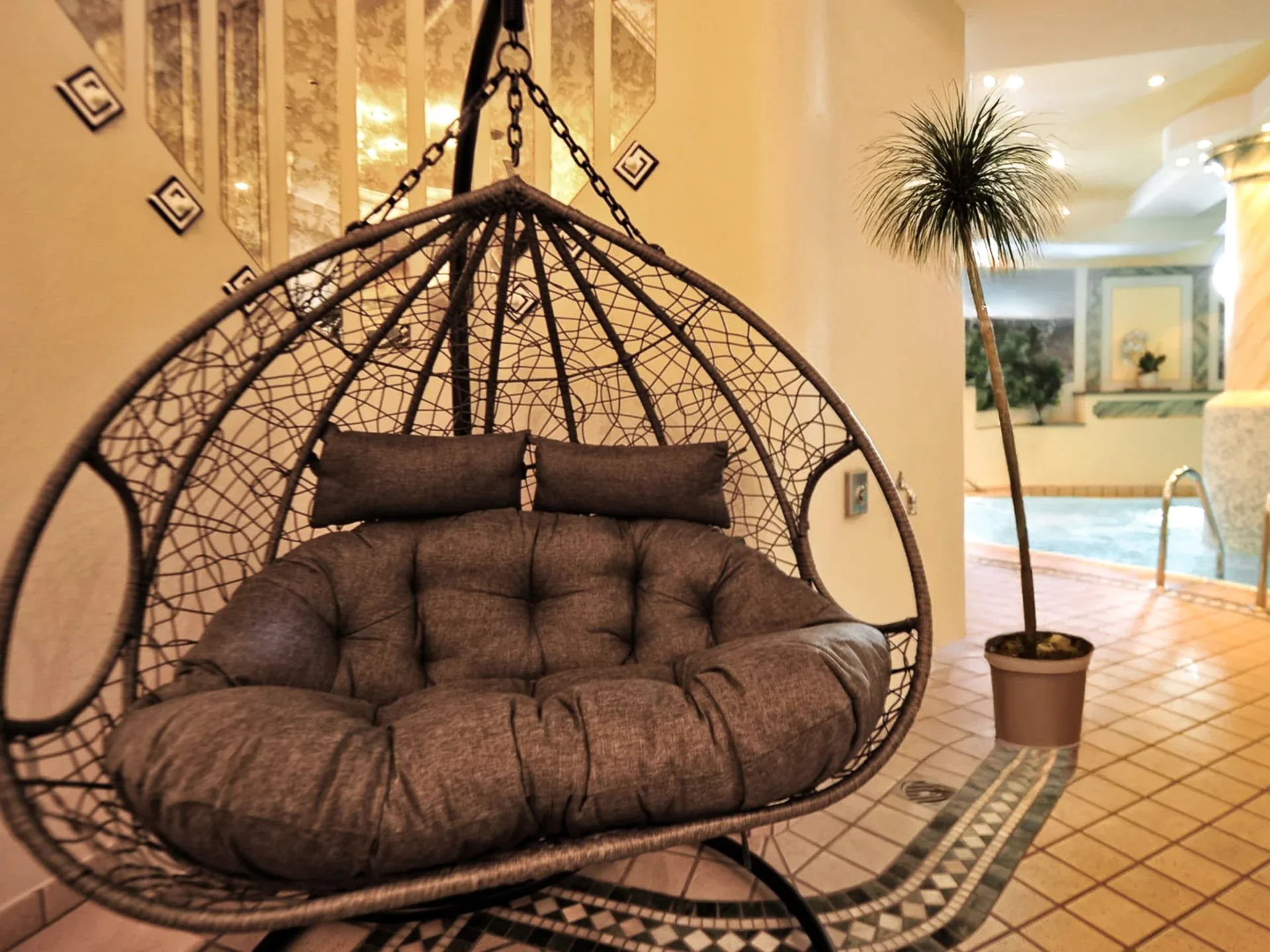 Die Bilder aus dem Hotel Salnerhof Hängesessel aus Korb mit Kissen neben Pool und Topfpflanze im Innenbereich