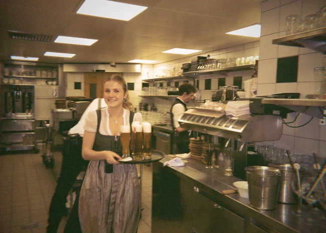 Dein Job im Salnerhof Lächelnde Kellnerin trägt Tablett mit Biergläsern in Restaurantküche