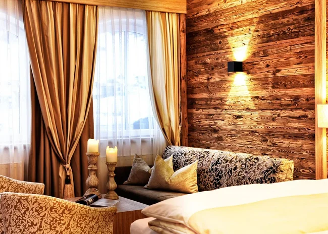 Der Salnerhof – das Hotel in Ischgl Gemütliches Hotelzimmer mit Holzverkleidung, Sofa, Sesseln und Kerzen