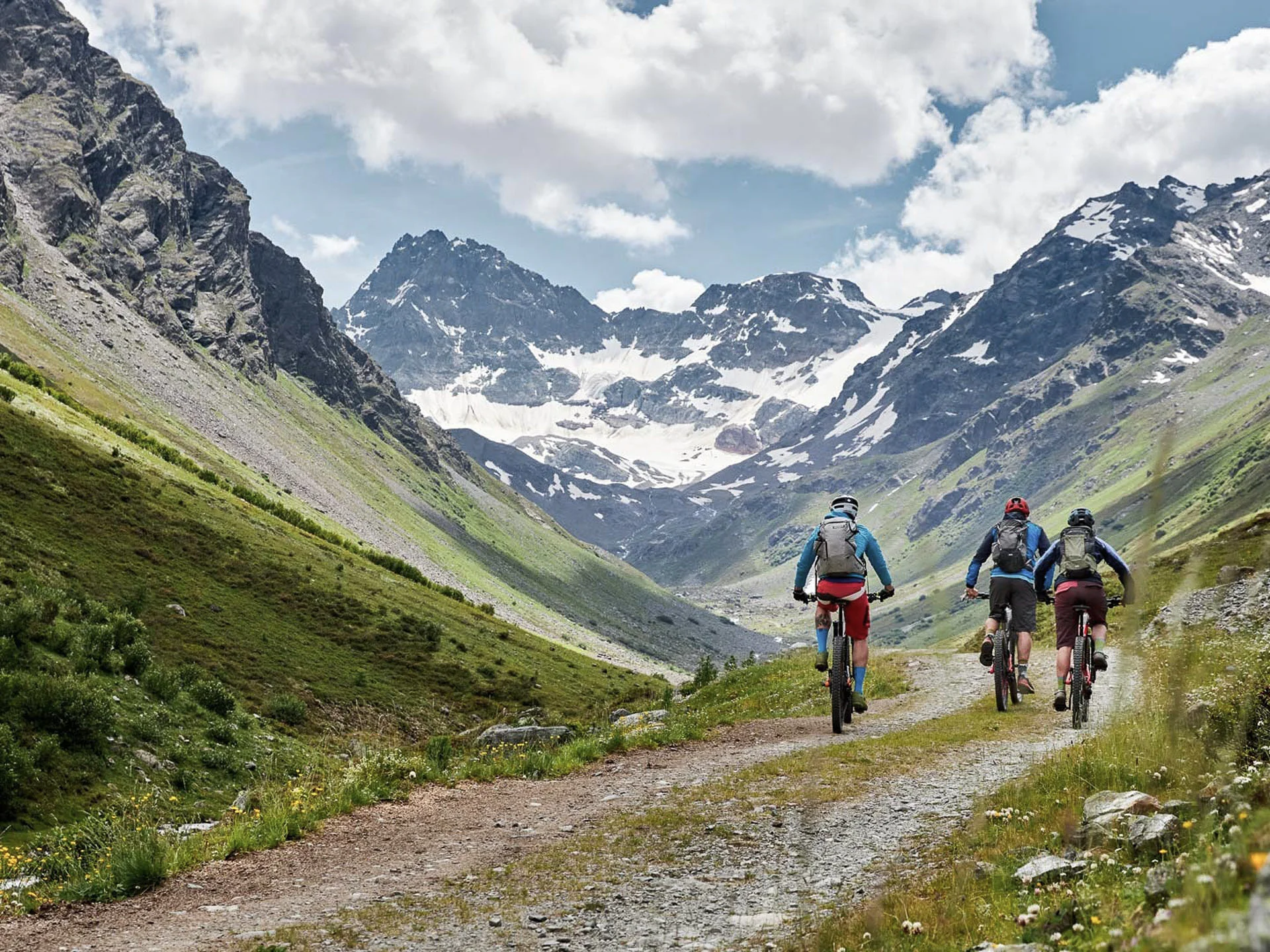 Die Bilder aus dem Hotel Salnerhof Drei Radfahrer fahren auf einem Bergweg mit schneebedeckten Gipfeln im Hintergrund