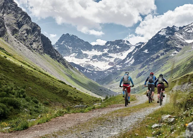 Ihr Sommer im Paznaun im Wander- und Bike-Hotel in Ischgl Drei Radfahrer fahren auf einem Bergweg mit schneebedeckten Gipfeln im Hintergrund