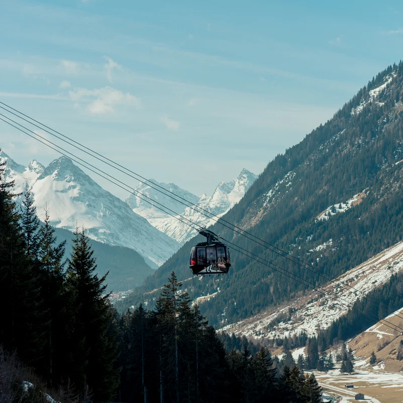Ihr Sommer im Paznaun im Wander- und Bike-Hotel in Ischgl Seilbahn über bewaldetes Tal mit schneebedeckten Bergen im Hintergrund