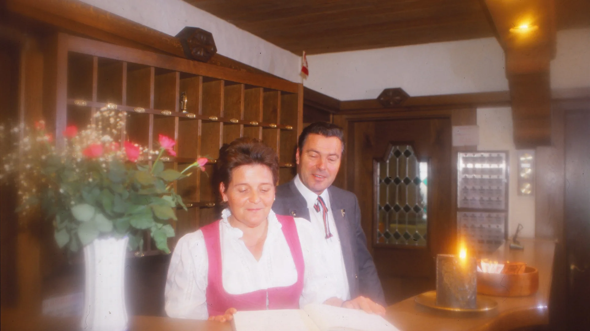 Die Geschichte des Salnerhofs Zwei Rezeptionisten an einem hölzernen Empfangstresen mit Blumen und Kerze
