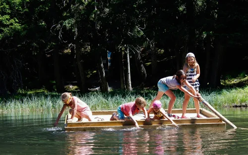 Kinder spielen auf einem Floß auf einem See vor einem Wald