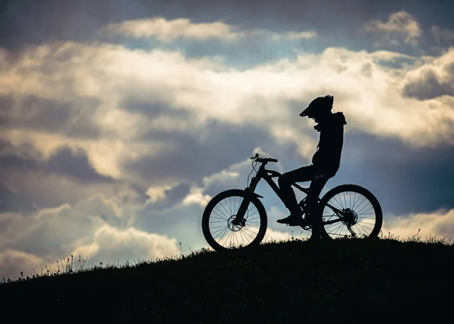 Ihr Sommer im Paznaun im Wander- und Bike-Hotel in Ischgl Silhouette eines Radfahrers mit Helm auf einem Hügel vor bewölktem Himmel