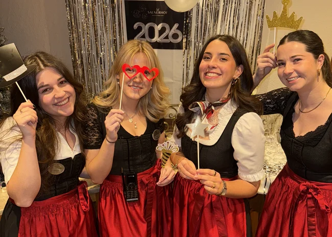 Dein Job im Salnerhof Vier Frauen in traditionellen Trachten posieren mit Partyrequisiten vor 2026 Dekoration