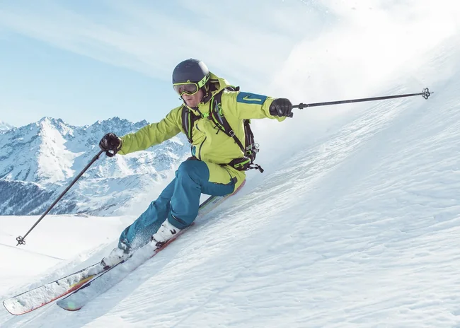 Der Salnerhof – das Hotel in Ischgl Skifahrer in grüner Jacke fährt auf verschneitem Hang mit Bergen im Hintergrund
