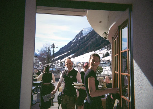 Dein Job im Salnerhof Fröhliche Kellner bedienen Gäste auf sonniger Terrasse mit Bergblick