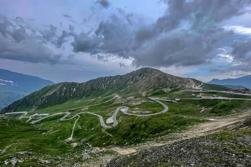 Ihr Sommer im Paznaun im Wander- und Bike-Hotel in Ischgl Serpentinenstraße auf grünem Berg unter bewölktem Himmel