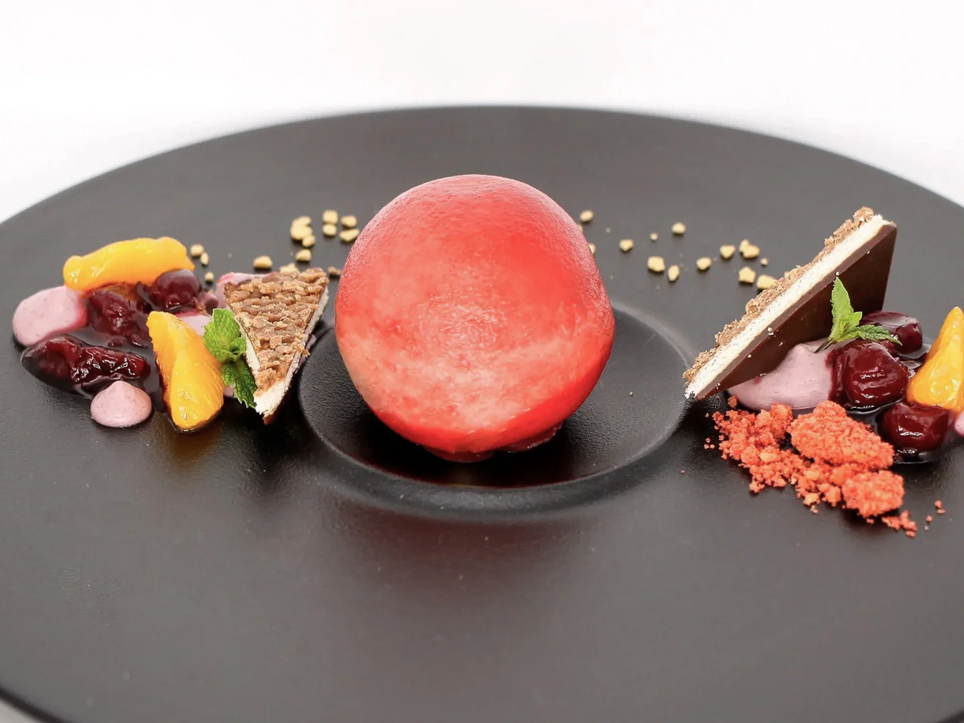 Die Bilder aus dem Hotel Salnerhof Rote Kugel Dessert mit Fruchtstücken und Schokoladentafel auf schwarzem Teller