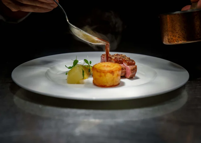 Kellner mit Inkasso Soße wird auf ein fein angerichtetes Gericht mit Fleisch und Beilage gegossen